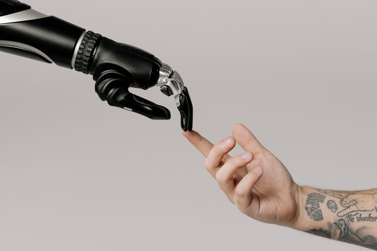 Home A human hand with tattoos reaching out to a robotic hand on a white background.